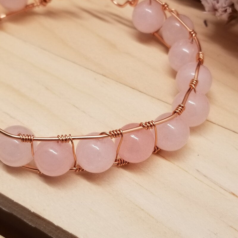 Pink beaded bracelet with rose gold wire on a wooden surface