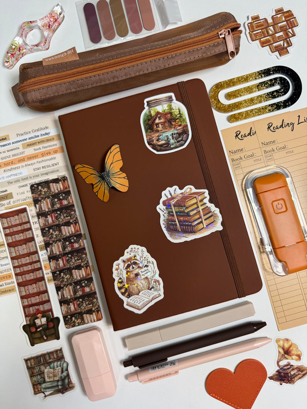 Brown notebook with stickers surrounded by stationery items on a white background