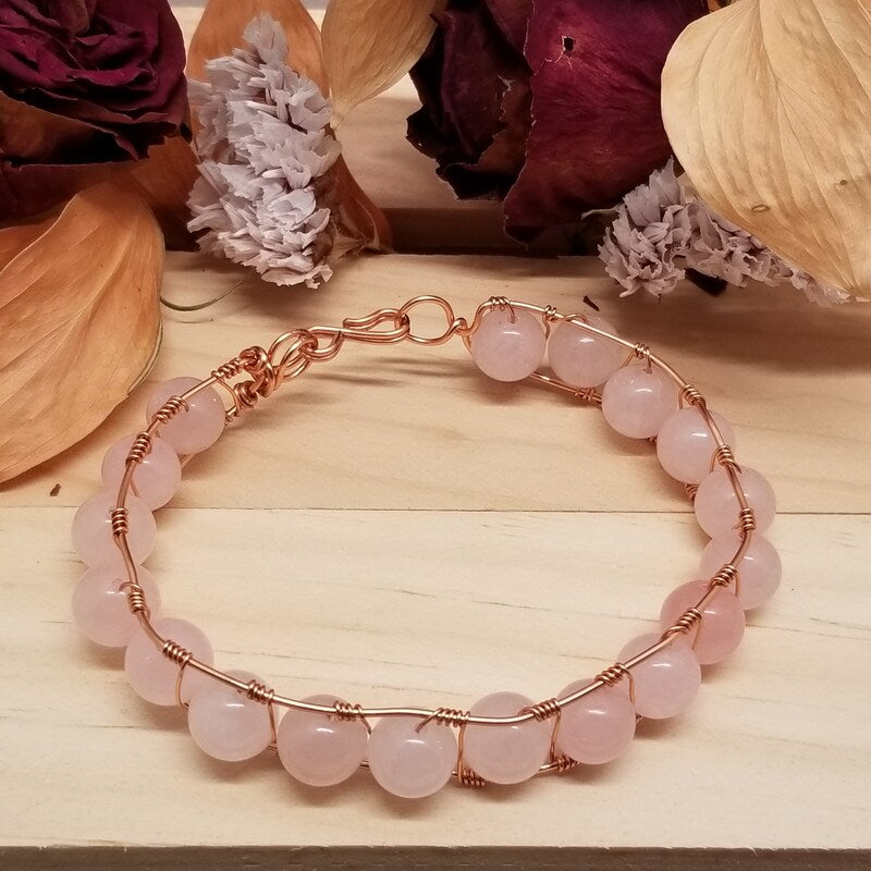 Rose gold bracelet with pink beads on a wooden surface with flowers in the background