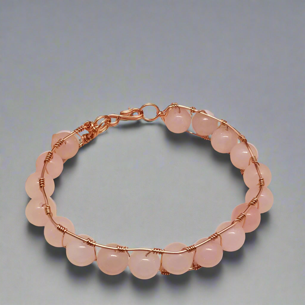 Pink beaded bracelet with rose gold wire wrapping on a gray background