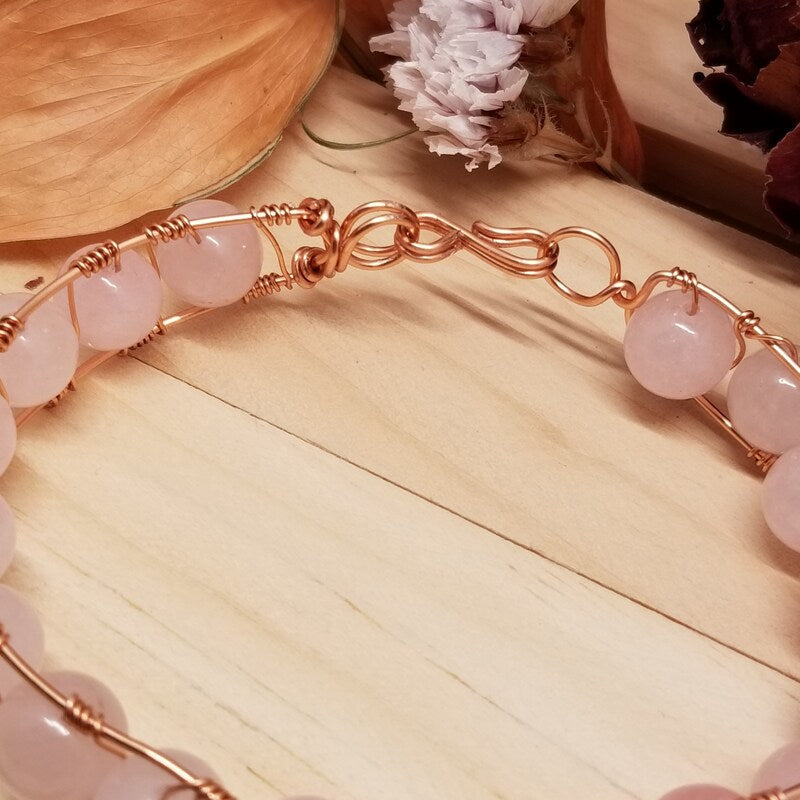 Bracelet with pink beads and rose gold wire on a wooden surface