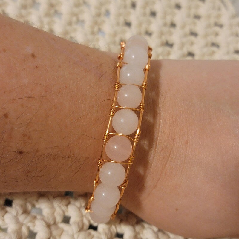 Bracelet with pink beads and gold wire on a wrist against a textured background