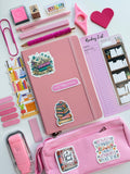 Pink stationery items including a notebook, pen, and pencil case with stickers on a white background.