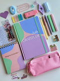 Stationery items including a gratitude journal, pink pencil case, and colorful markers on a white background.