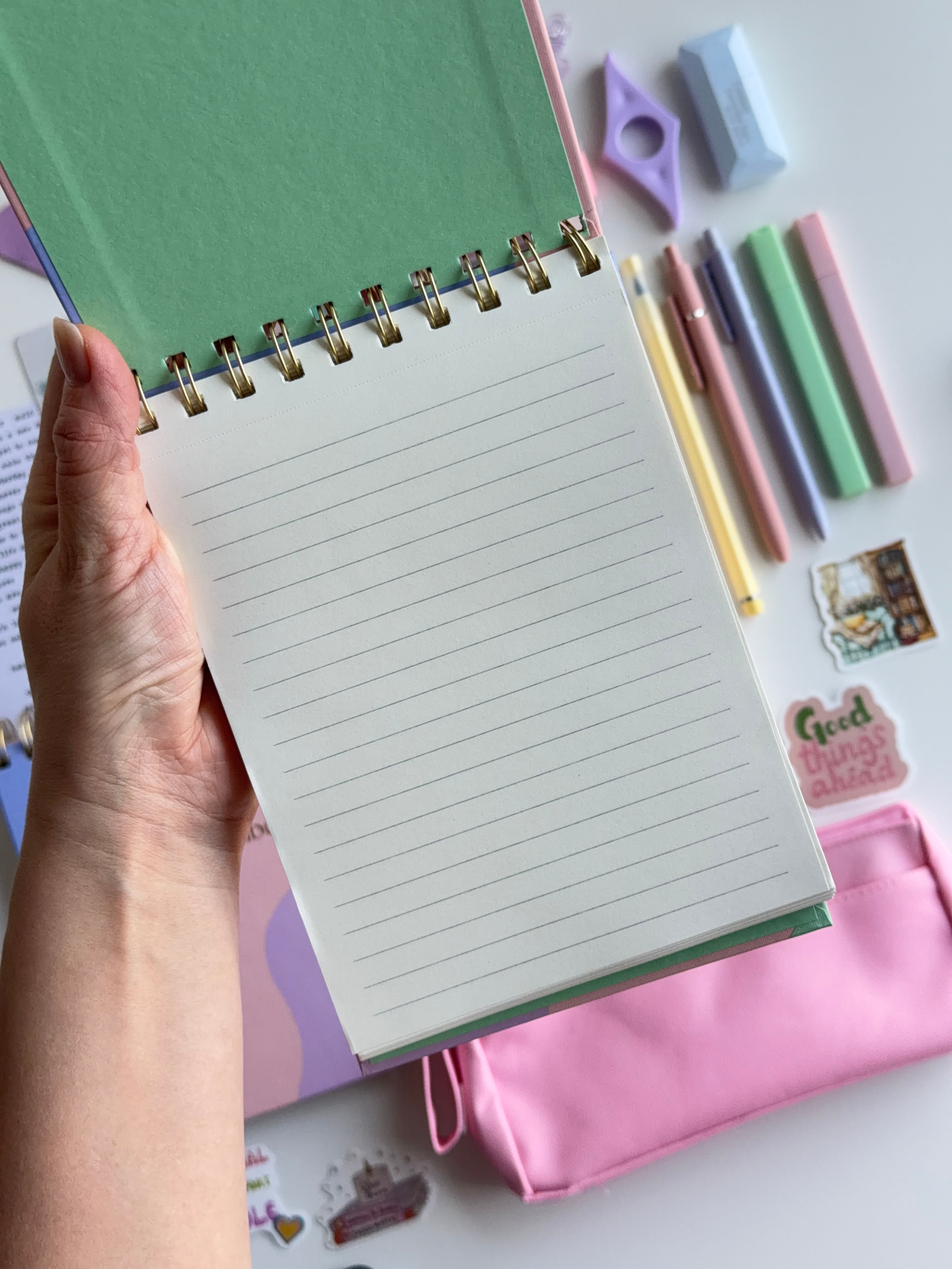 Hand holding a spiral-bound notebook with stationery items on a white background