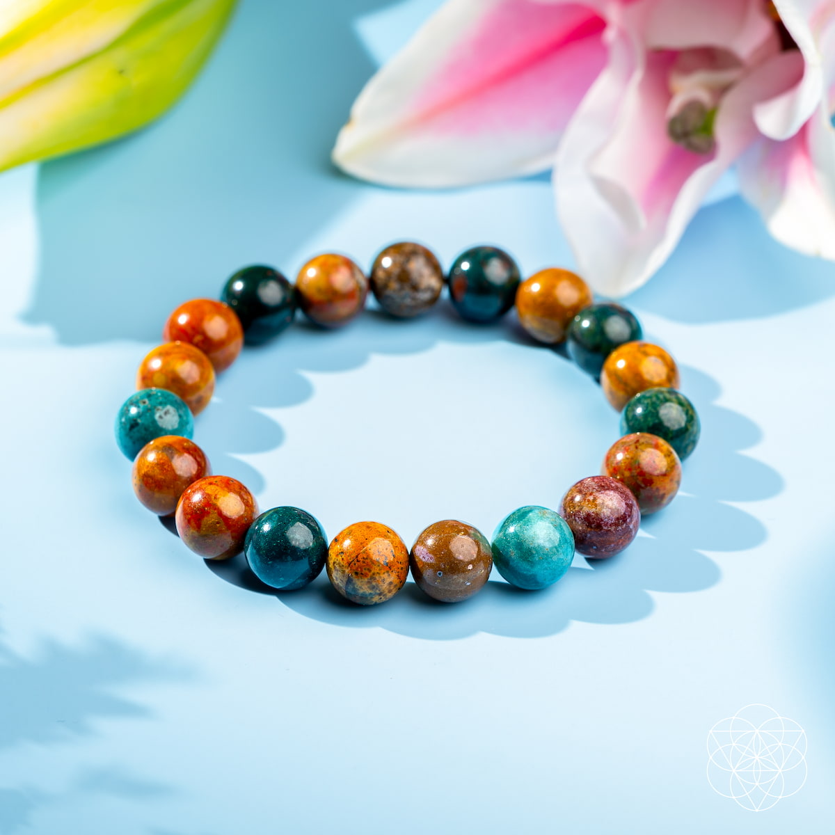 Multicolored beaded bracelet on a light blue surface with flowers in the background