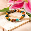 Multicolored beaded bracelet on a wooden surface with pink flowers in the background