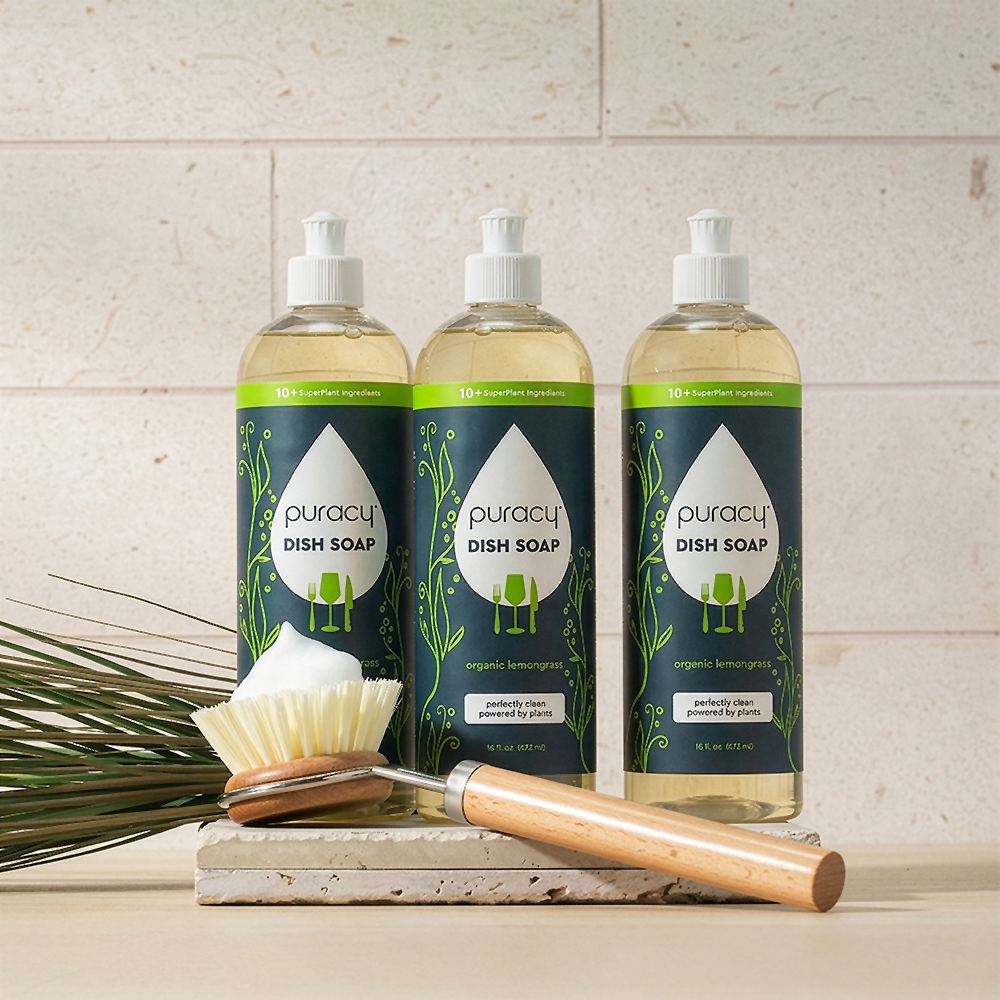 Three bottles of Puracy dish soap on a kitchen counter with a scrubber and paper towel.