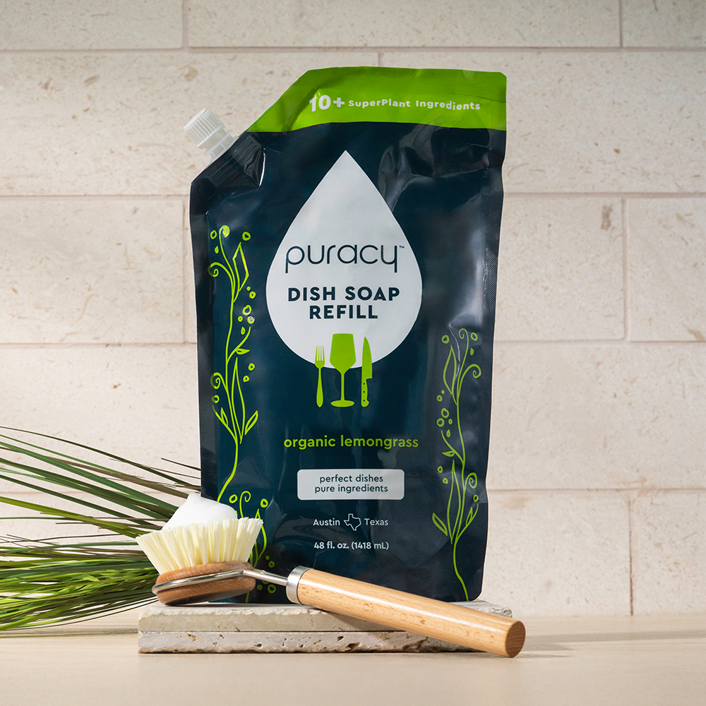 Puracy dish soap refill package with a brush and lemongrass plant on a light background