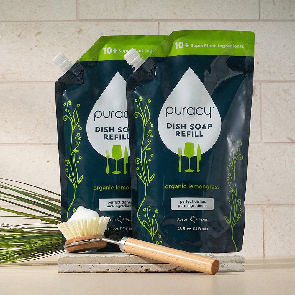 Two puracy dish soap refills with a scrubbing brush on a neutral background