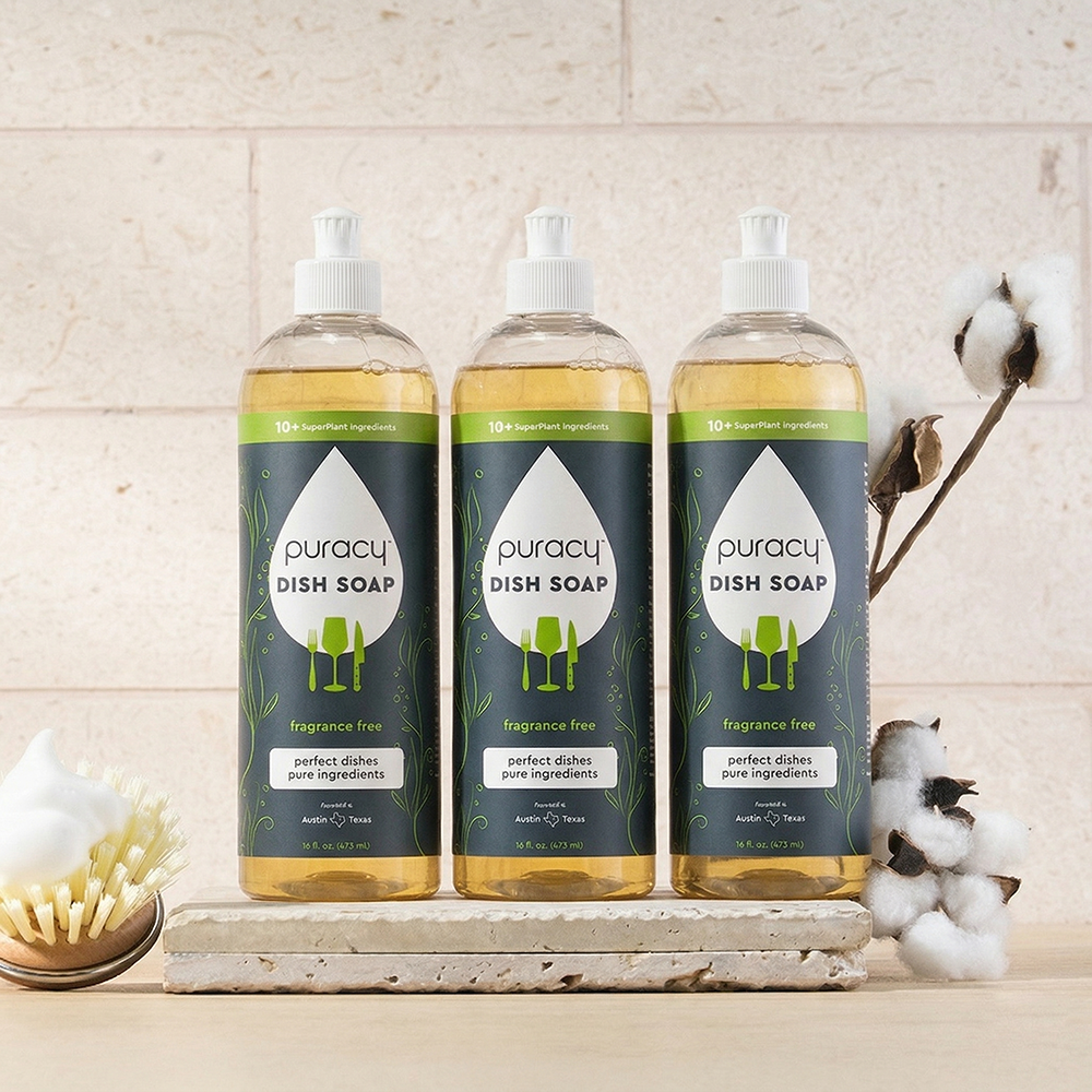 Three bottles of puracy dish soap on a wooden surface with a neutral background