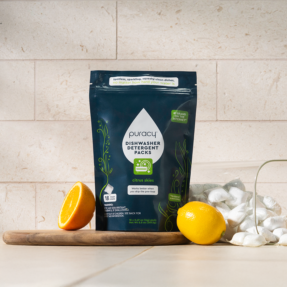 Puracy dishwasher detergent packs on a kitchen counter with lemons and oranges.