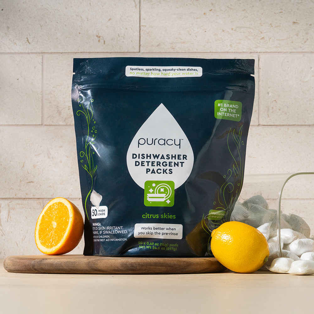 Puracy dishwasher detergent packs with lemons and an orange on a wooden cutting board.
