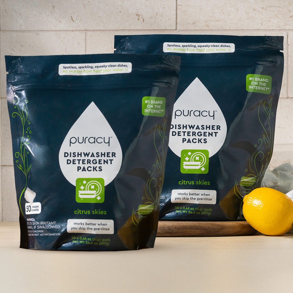Two packages of Puracy dishwasher detergent packs on a countertop with a lemon.
