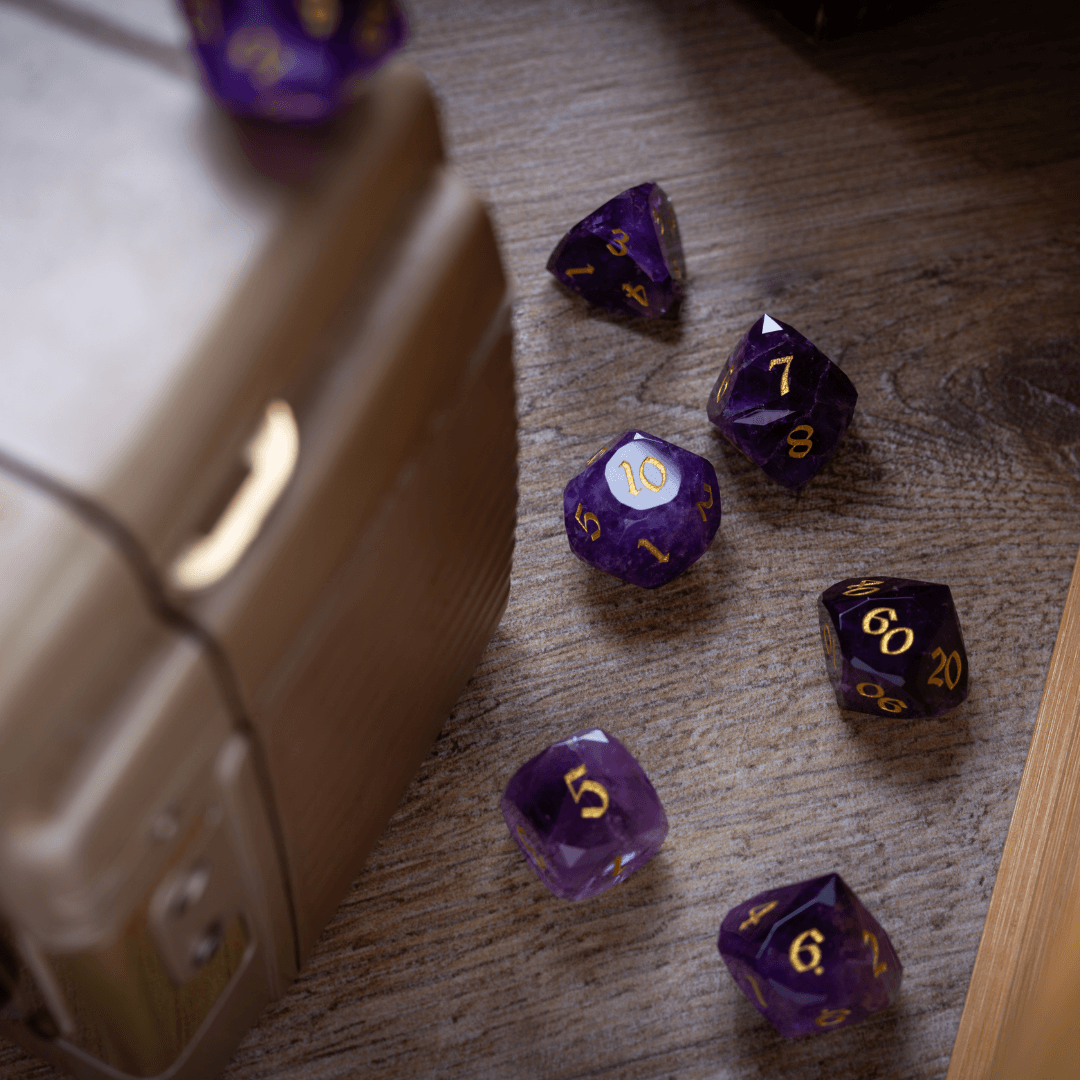 Purple polyhedral dice with gold numbers on a wooden surface next to a beige dice container.