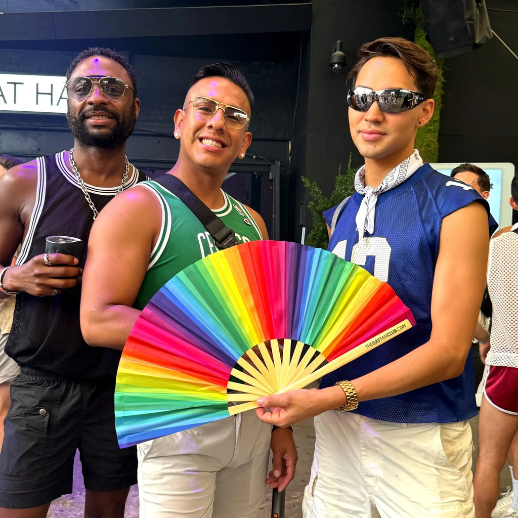 Three men posing with a colorful fan at an outdoor event.