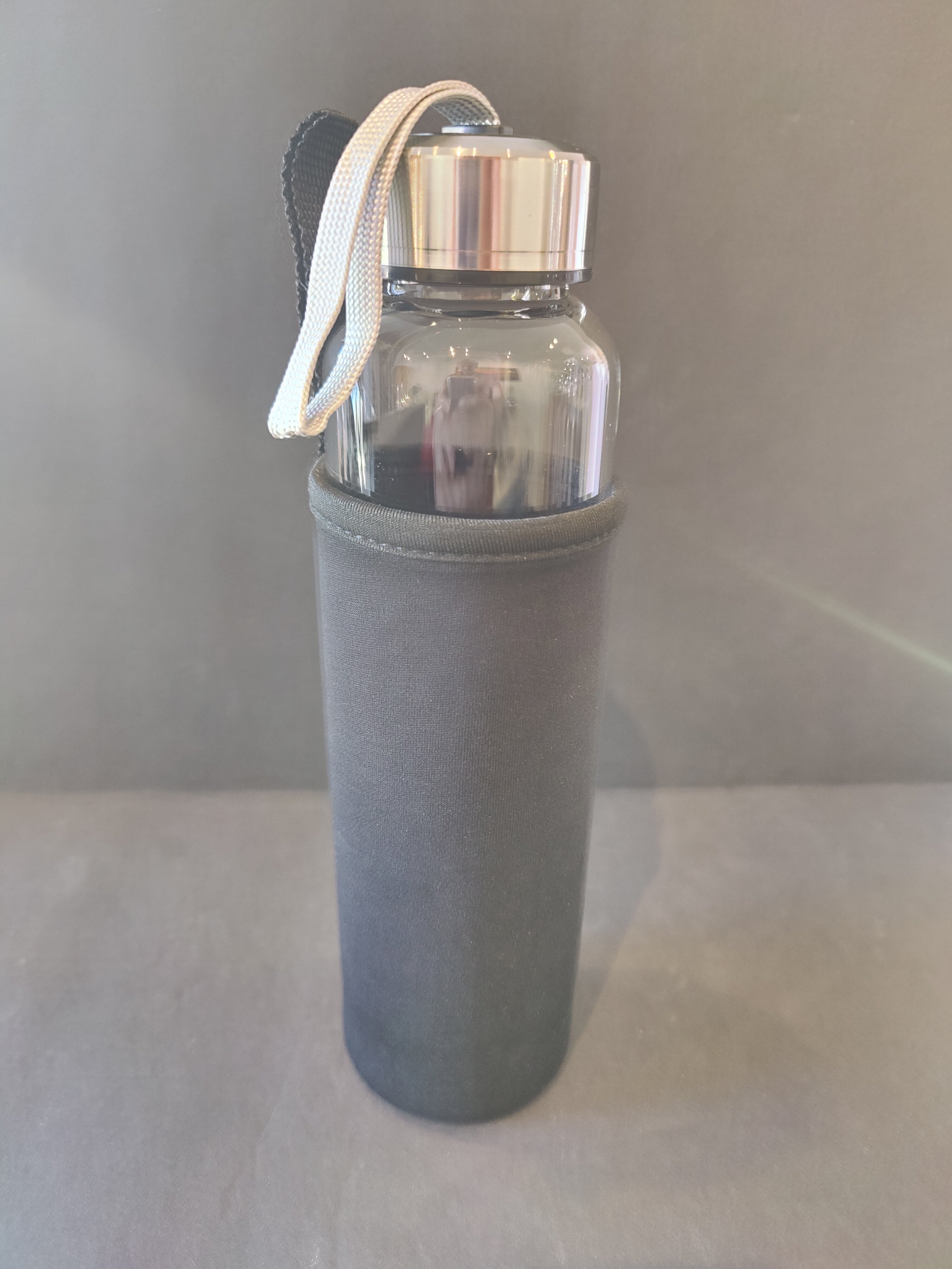 Clear water bottle 16oz with silver caps containing crystals and an insulated bottle cover on a gray surface.