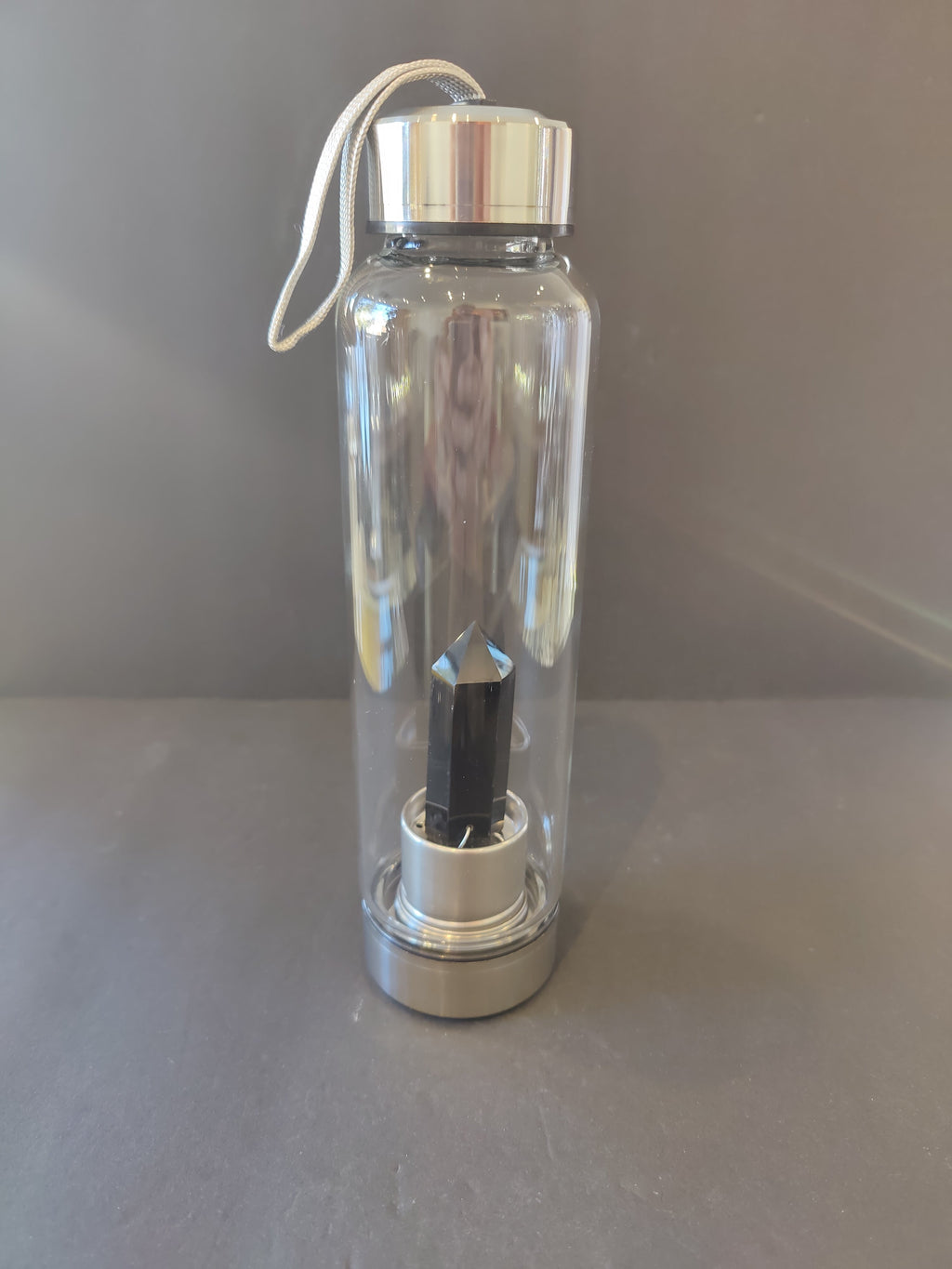 Clear water bottle with silver cap with a black crystal inside on a gray surface