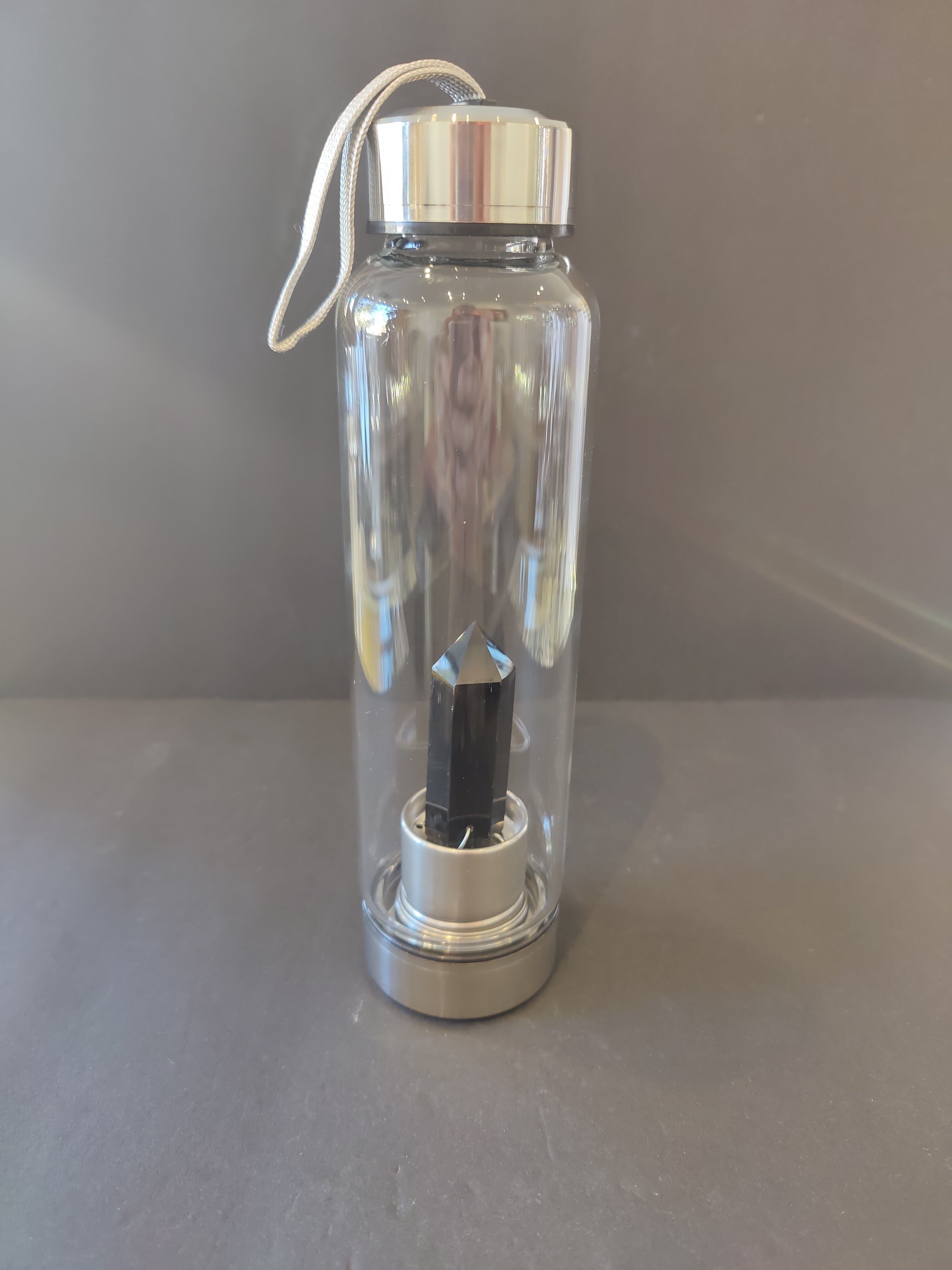 Clear water bottle with silver cap with a black crystal inside on a gray surface