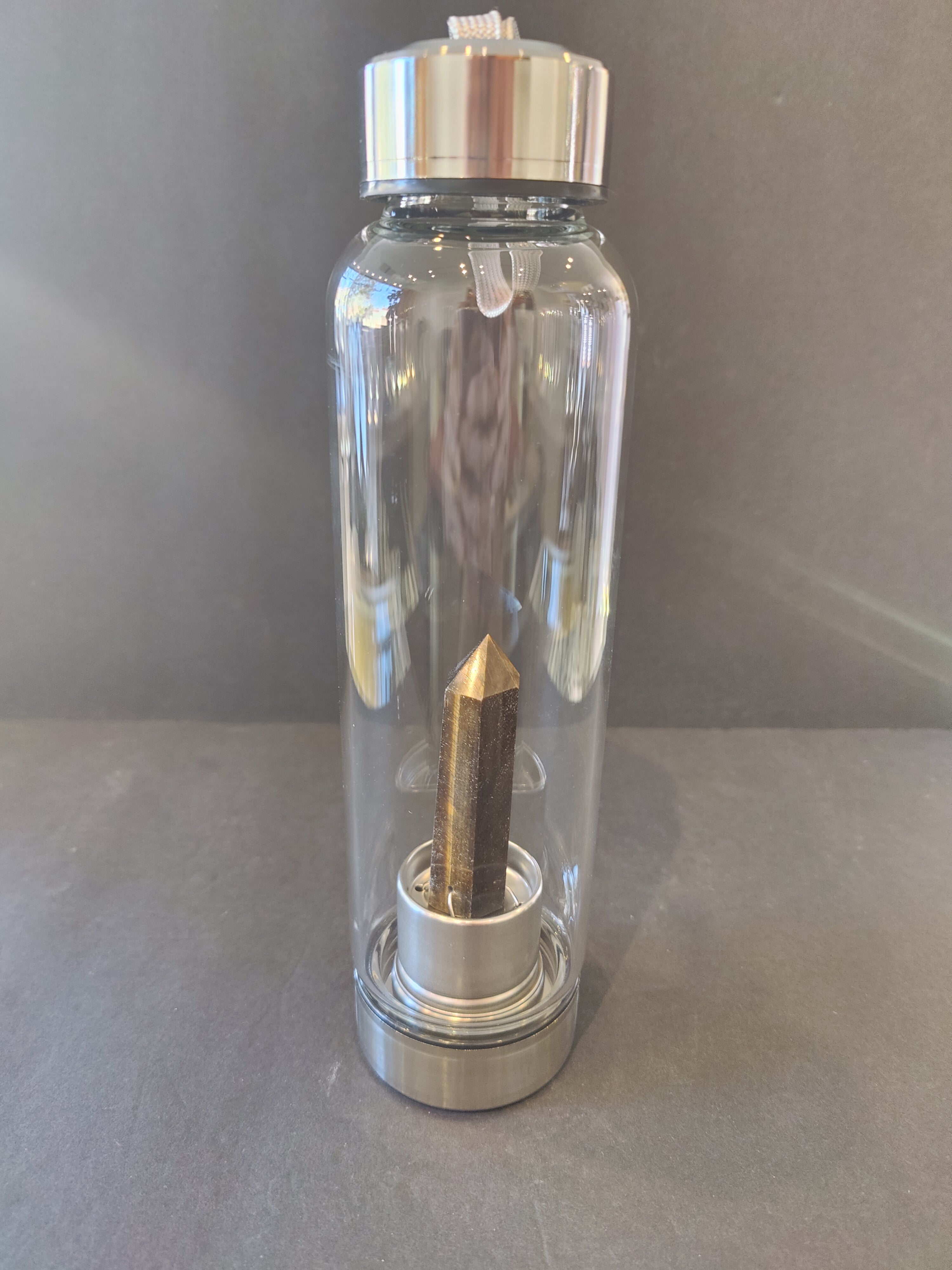 Clear water bottle with silver cap and brown crystal inside on a gray background