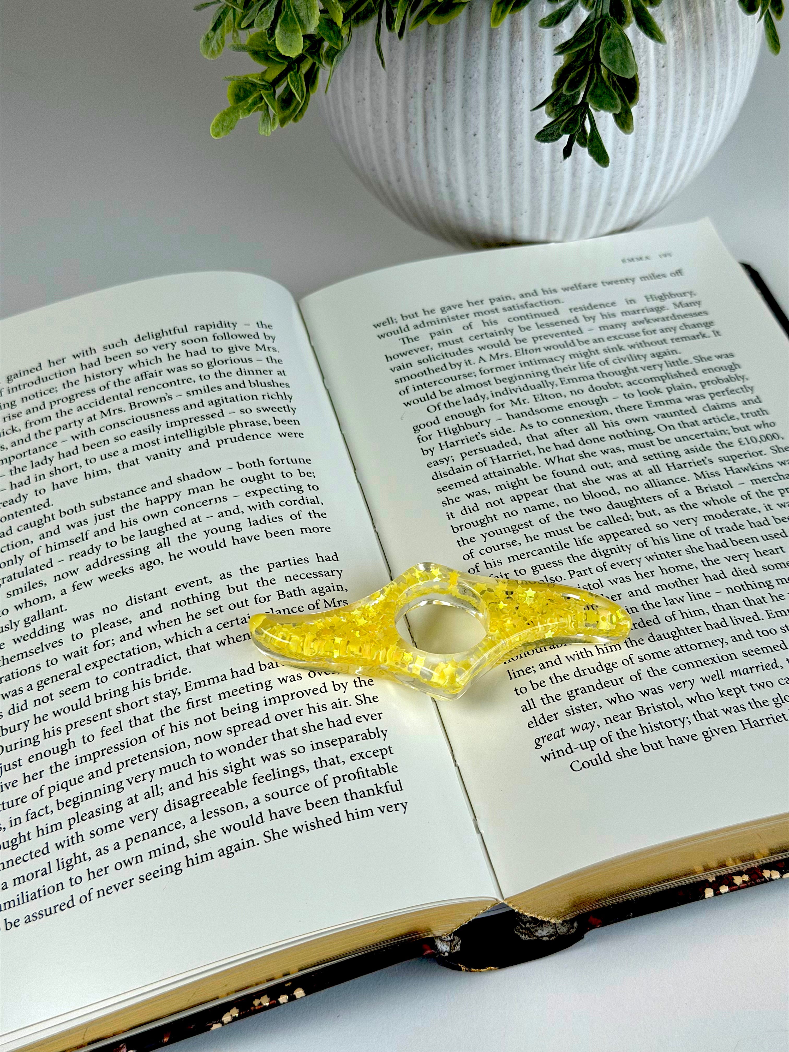 Open book with a decorative yellow clip on a white surface with a plant in the background