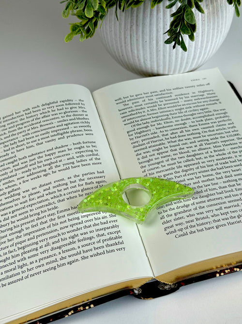 Open book with a green leaf-shaped object on top, next to a potted plant.