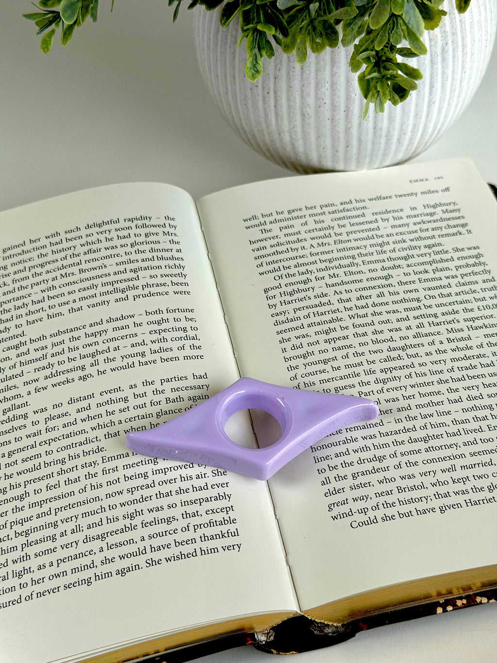 Open book with a purple page marker on a white surface, next to a potted plant.