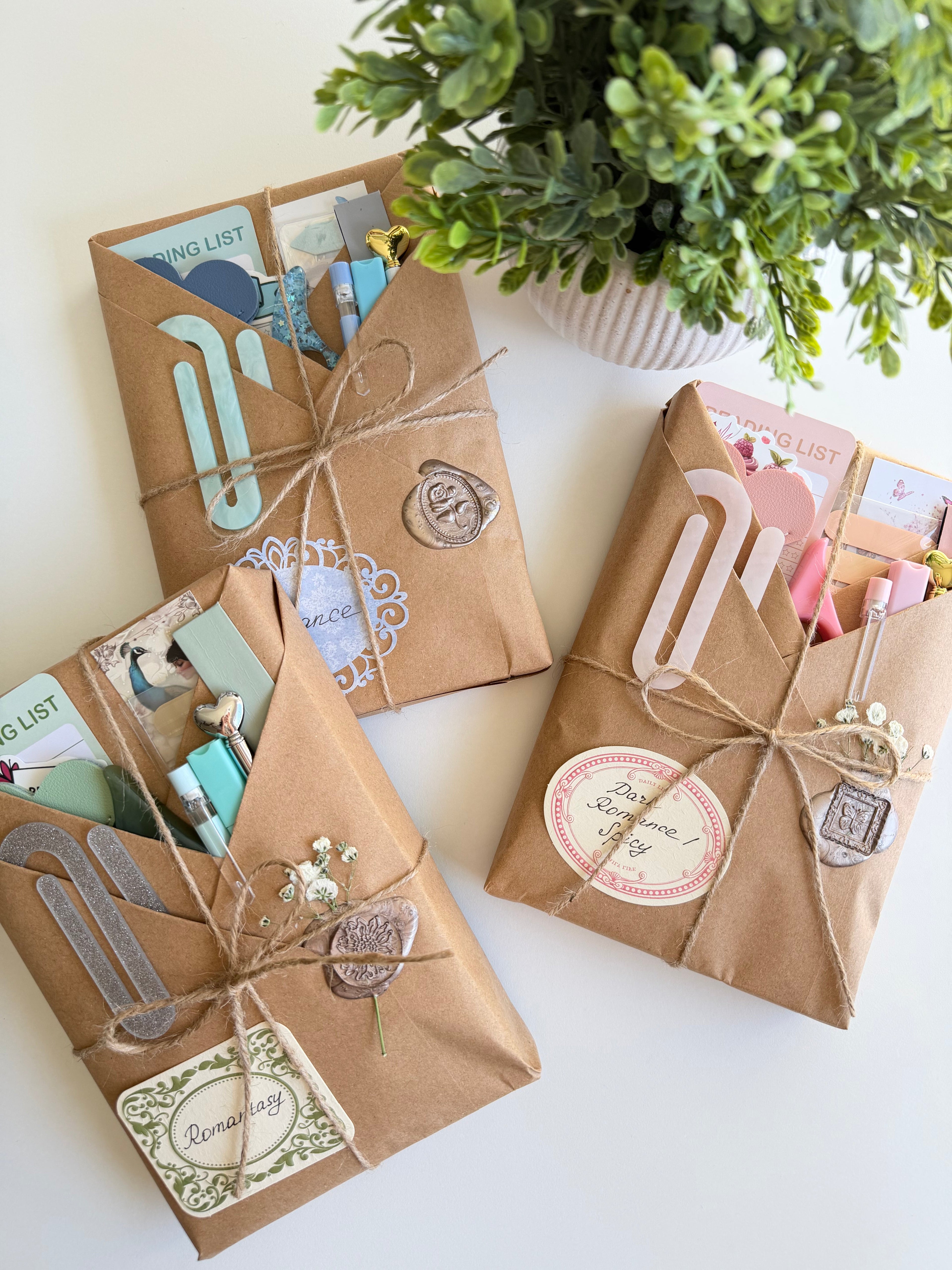 Three brown paper-wrapped packages with decorative elements on a white surface with a plant in the background.