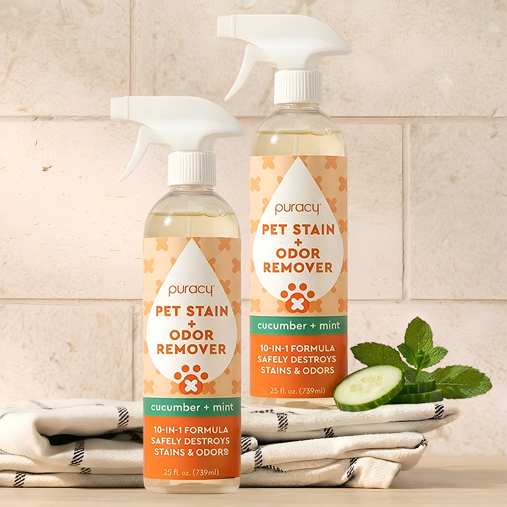 Two bottles of Puracy Pet Stain + Odor Remover on a kitchen counter with cucumbers and mint leaves.