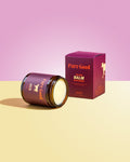 Jar of 'Pure Good' balm with packaging on a pink and yellow gradient background