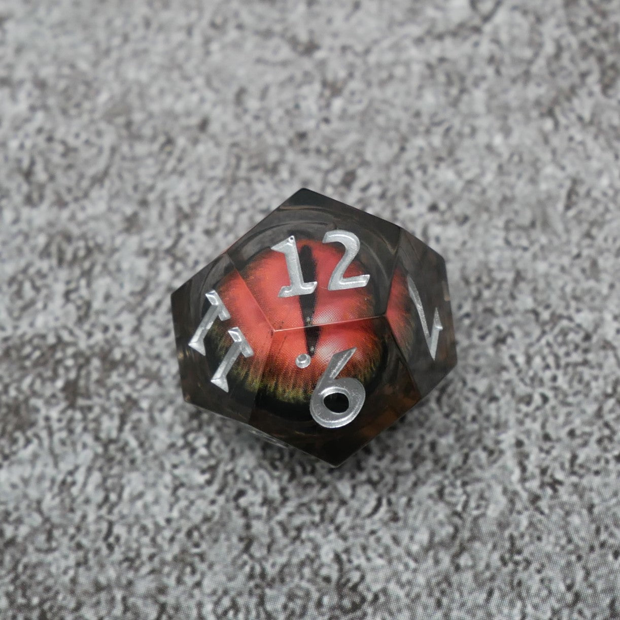 Dodecahedral dice with red and black design on a textured gray surface
