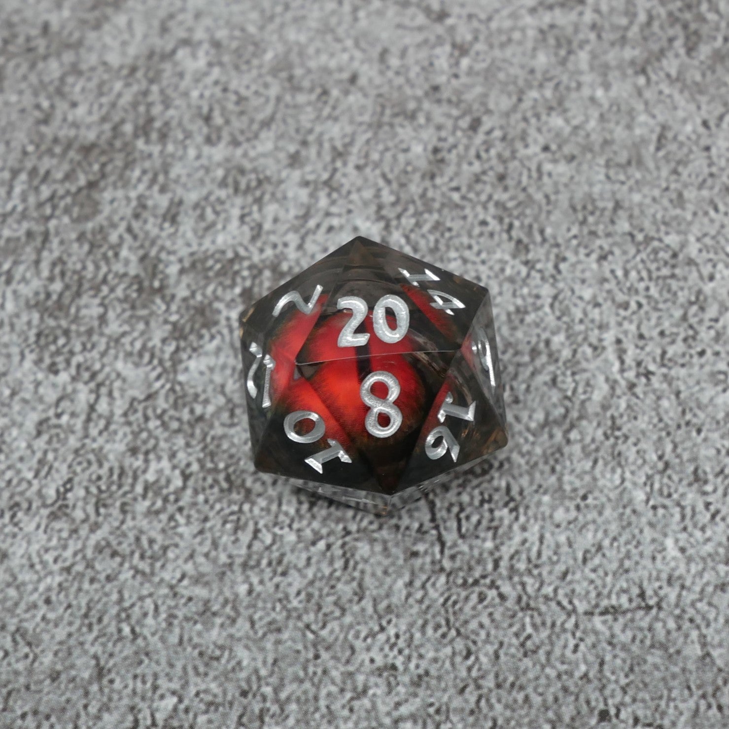 D20 polyhedral dice with red and black design on a gray surface