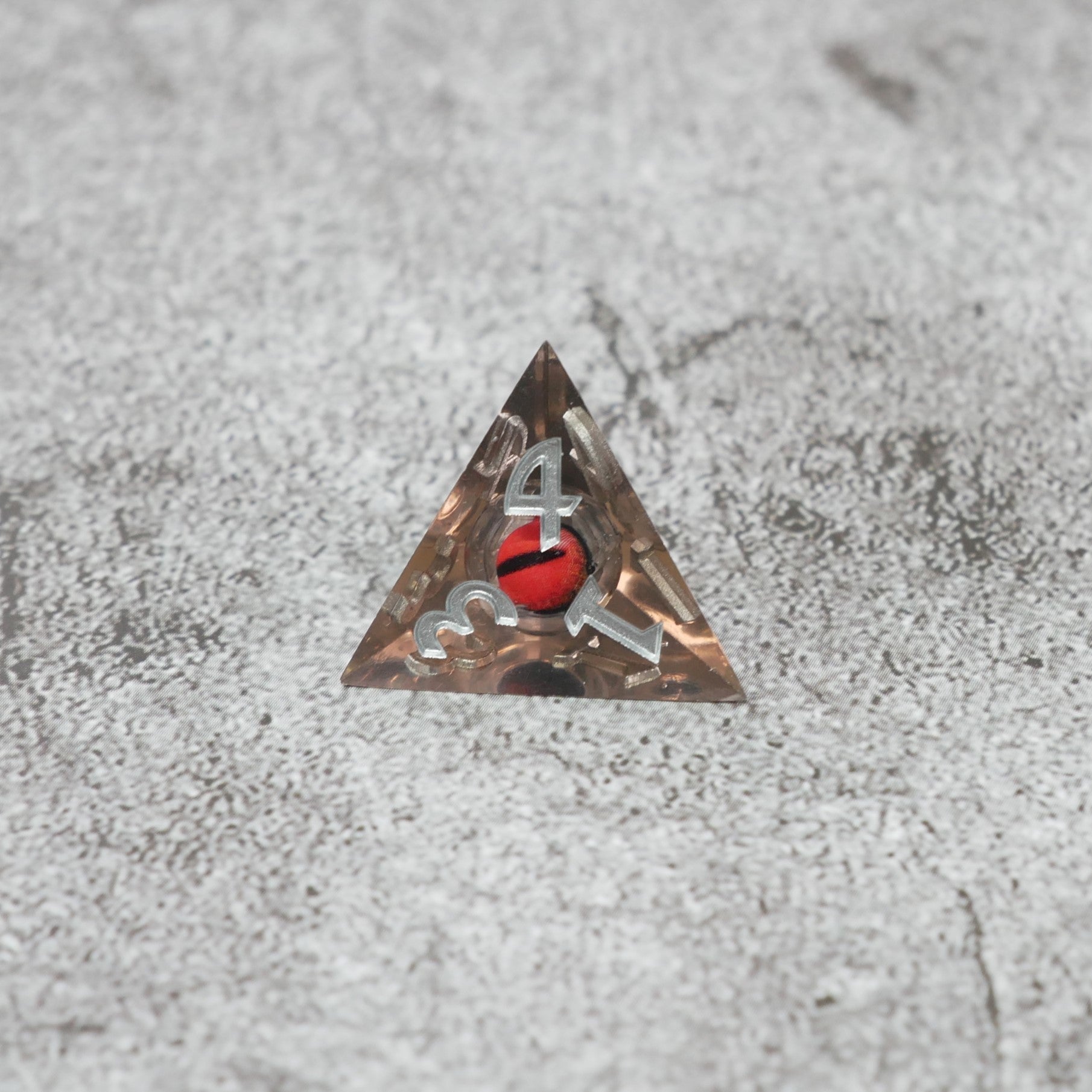 Triangular metal badge with a red and black design on a textured gray surface