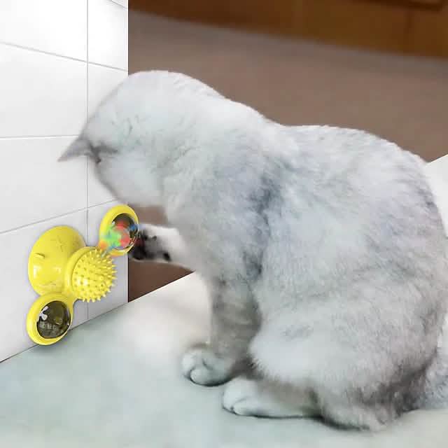 Cat playing with a yellow pet toy on a tiled floor.