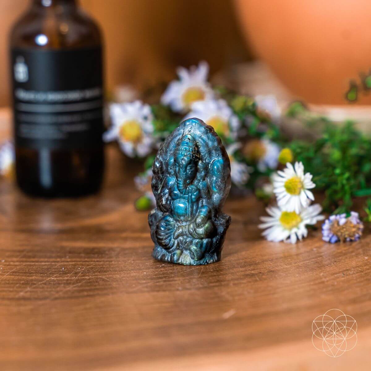 Labradorite stone figurine on a wooden surface with flowers and a bottle in the background
