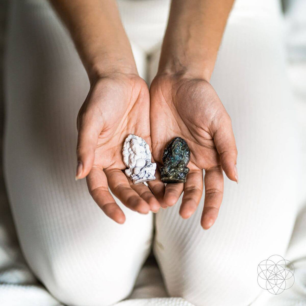 Two hands holding two different crystals against a neutral background