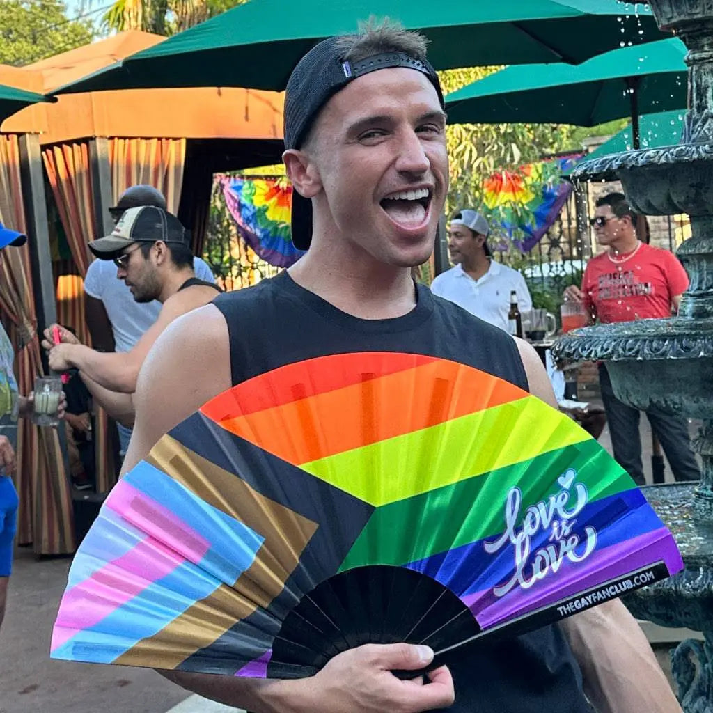 Person holding a rainbow-colored fan with 'Love is Love' text at an outdoor event.