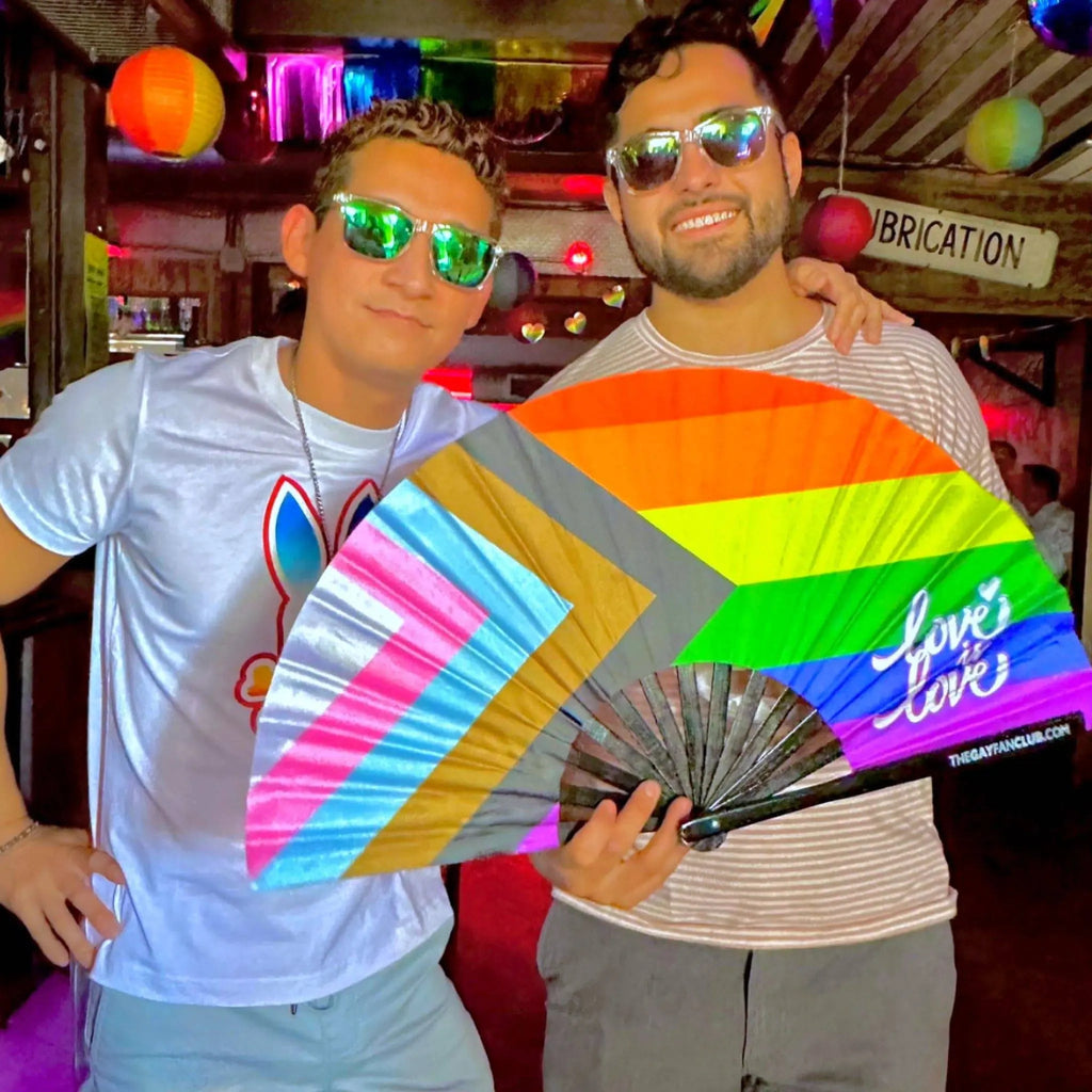 Two people holding a rainbow-colored fan with 'love' written on it in a festive indoor setting.