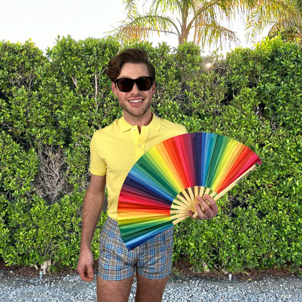 Man holding a colorful fan outdoors with greenery in the background