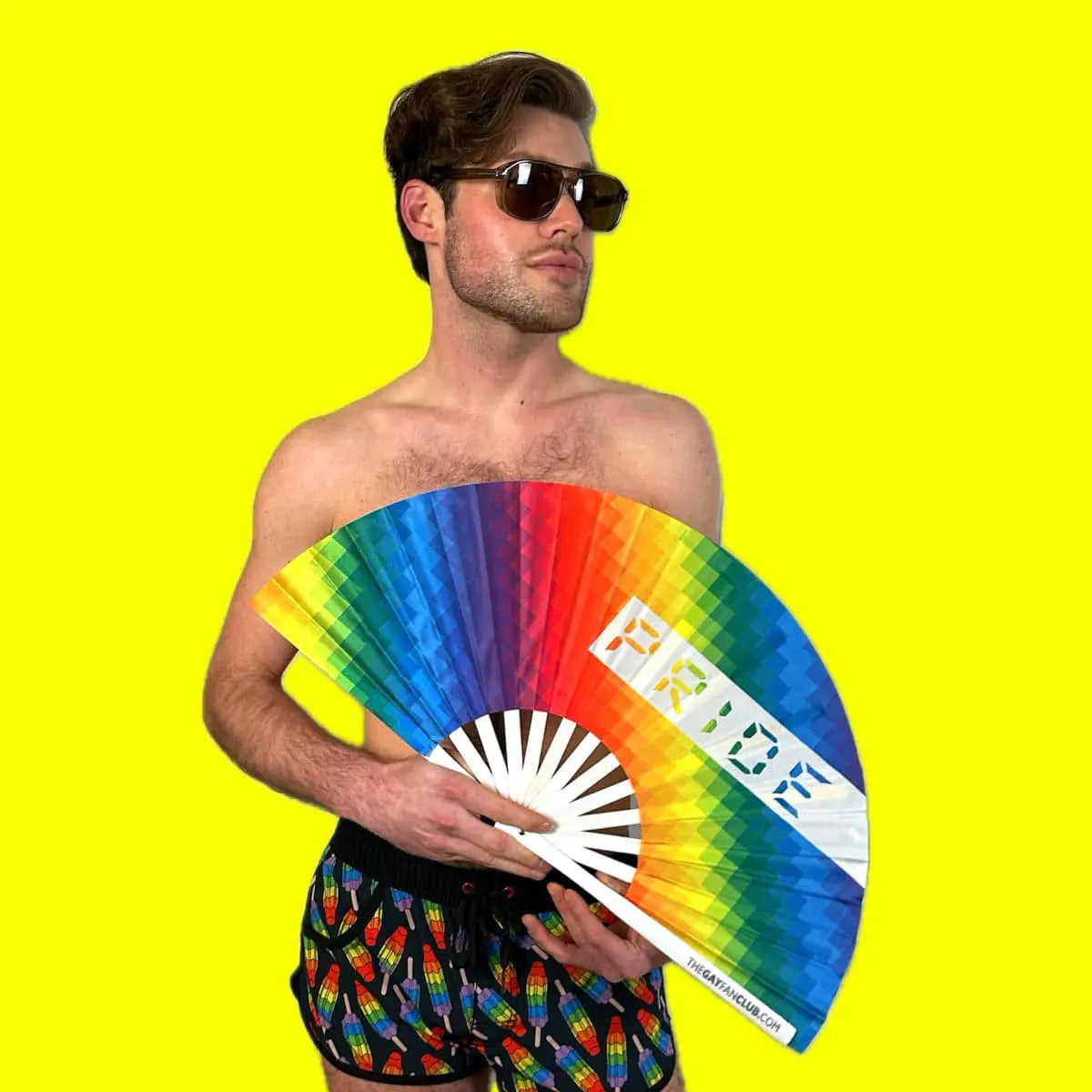 Man holding a rainbow-colored fan with 'PRIDE' text against a yellow background