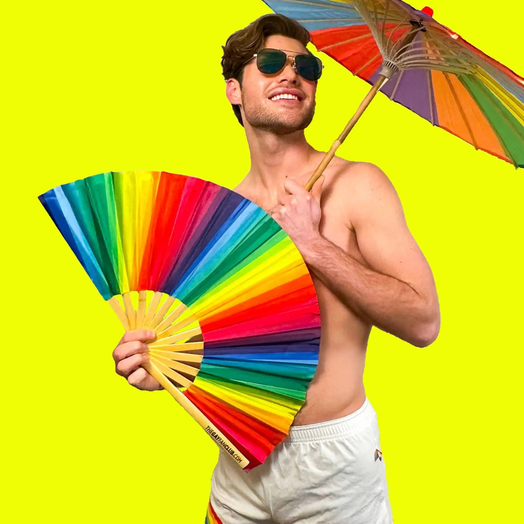 Man holding a rainbow-colored fan and umbrella against a bright yellow background
