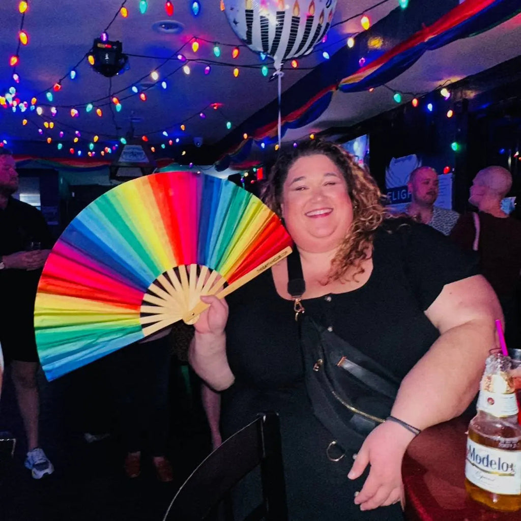 Person holding a colorful fan in a festive indoor setting with lights and people around.