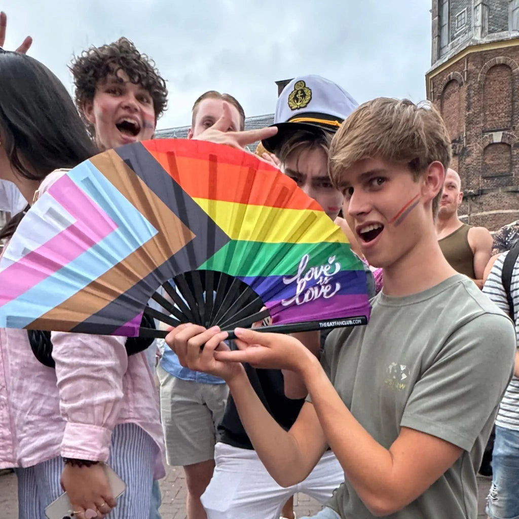 Person holding a rainbow flag with 'love is love' text in an outdoor setting.