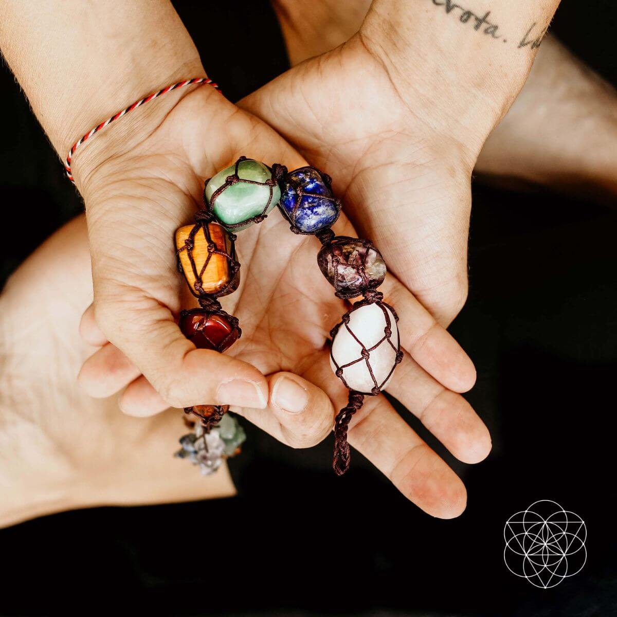 Hands holding a colorful crystal tassel against a dark background