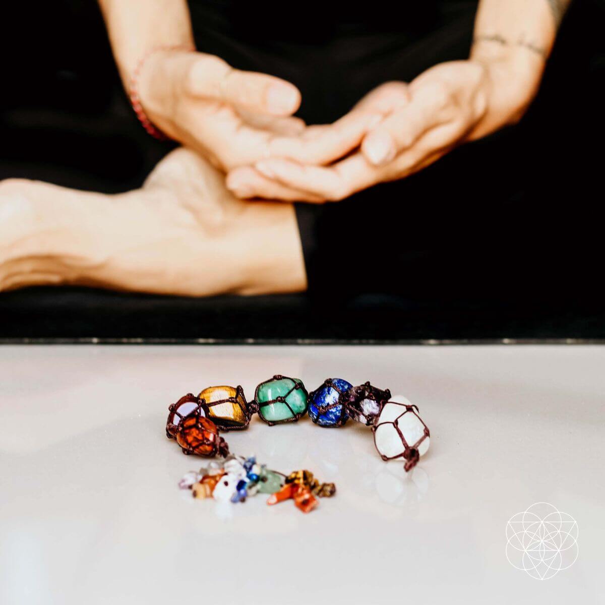 Colorful gemstones on a white surface with hands in the background