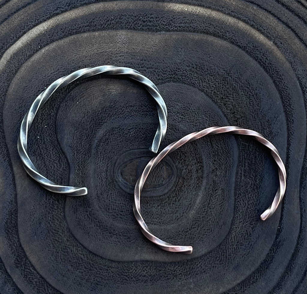 Two silver bracelets on a textured black surface