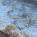 Pair of copper hoop earrings on a textured blue surface