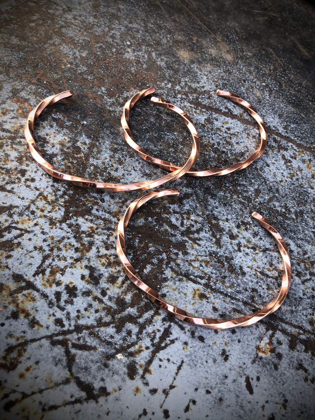 Three copper bracelets on a textured metal surface